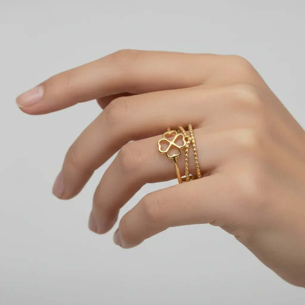 Gold Clover Triple Band Ring shown on a hand, featuring a smooth band, beaded detail, and a geometric clover design.