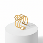 Gold Clover Triple Band Ring displayed on a pedestal, featuring layered smooth, beaded, and geometric designs.