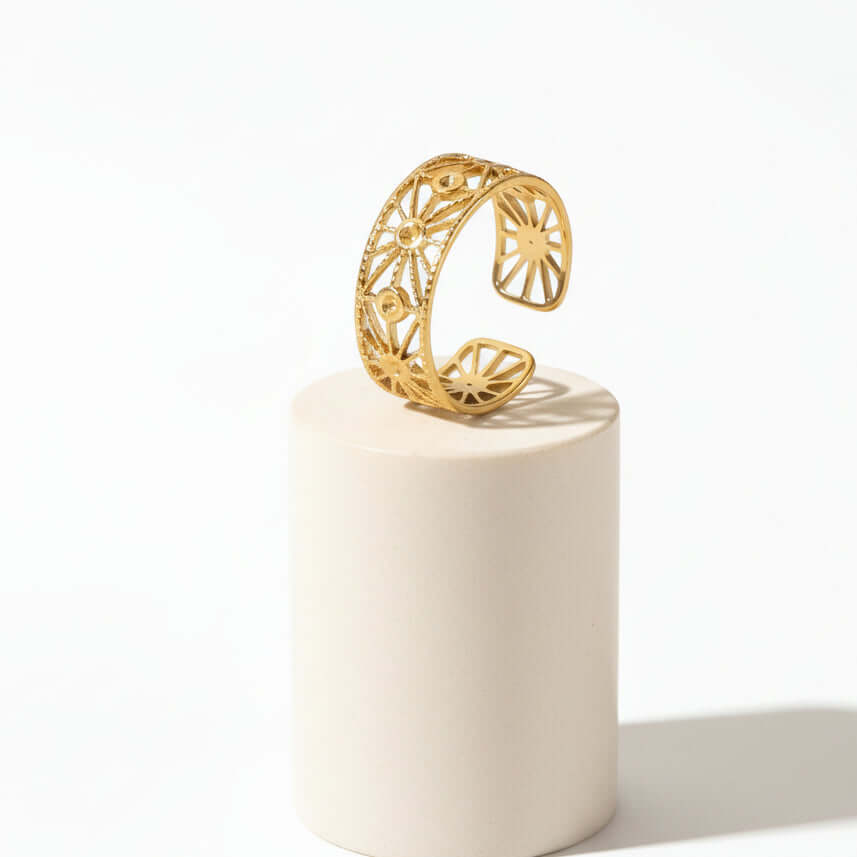Gold Cut Out Floral Ring displayed on a pedestal showcasing its intricate floral design and open-band silhouette.