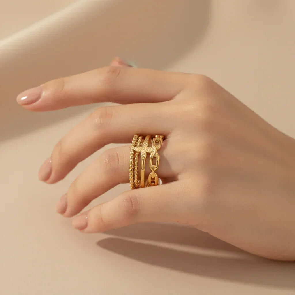 Woman's hand wearing multiple gold rings, Ceyrah jewelry close-up on neutral background
