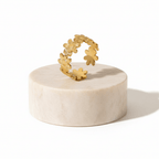Gold Floral Linked Ring displayed on a marble pedestal, showcasing its intricate flower design.