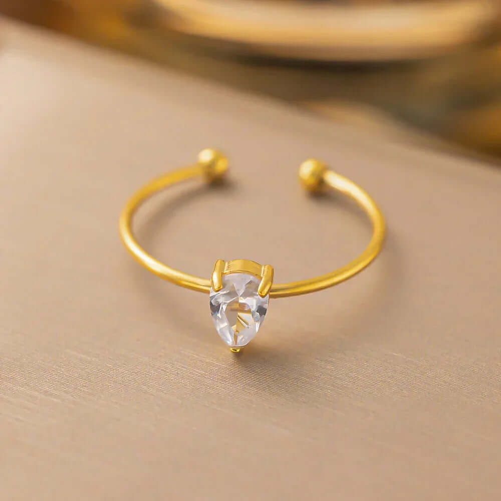 Ceyrah gold open ring with clear teardrop gemstone on beige background
