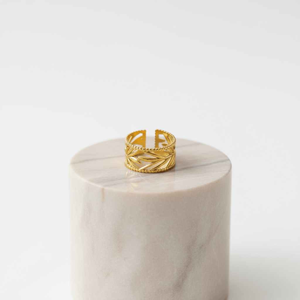 Leaf Etched Adjustable Ring displayed on a marble pedestal, showcasing its intricate golden leaf etching and adjustable design.