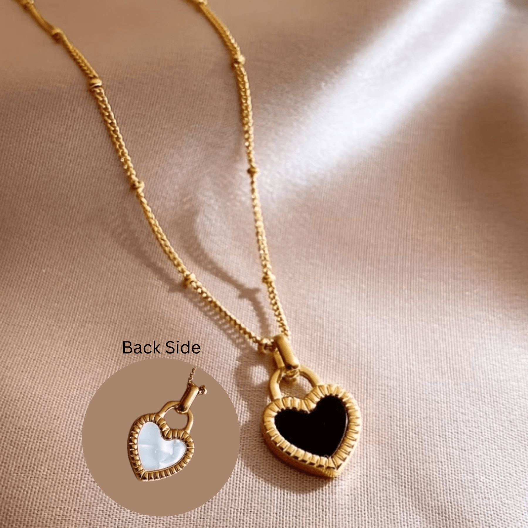 Gold heart pendant necklace with black and white reversible charm on satin background