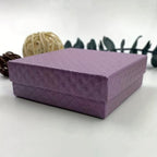 On a white surface with decorative elements in the background display Purple Gift box with necklace