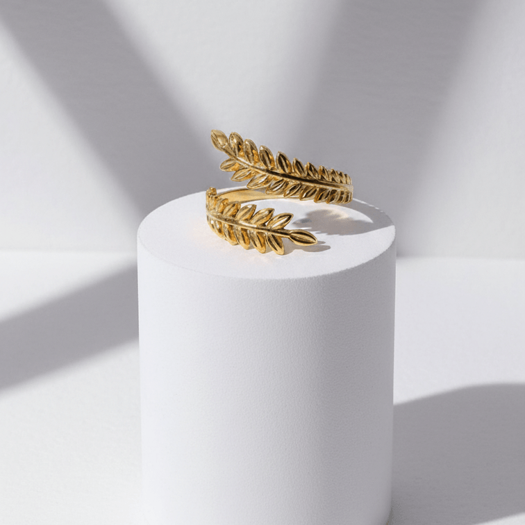 Aurelia Leaf Adjustable Gold Ring on a white cylindrical stand with a light gray background