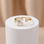 Dainty Bloom Open Gold Adjustable Ring on a white cylindrical stand against a beige background