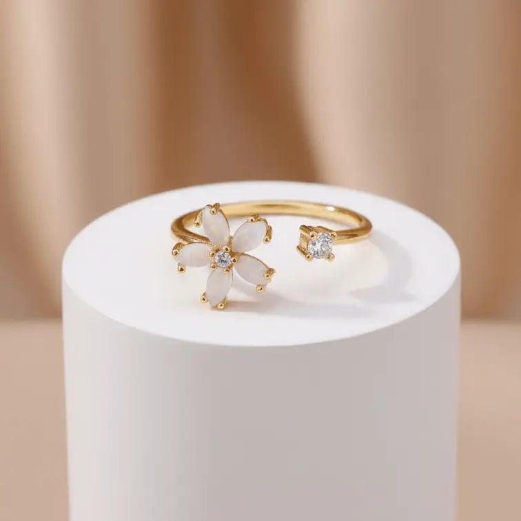 Dainty Bloom Open Gold Adjustable Ring on a white cylindrical stand against a beige background