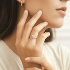 Close-up of a woman's hand wearing a Dainty Bloom Open Gold Adjustable Ring with a diamond, touching her face.