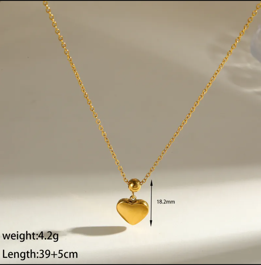 Gold heart pendant necklace on a delicate gold chain, displayed against a light beige background 