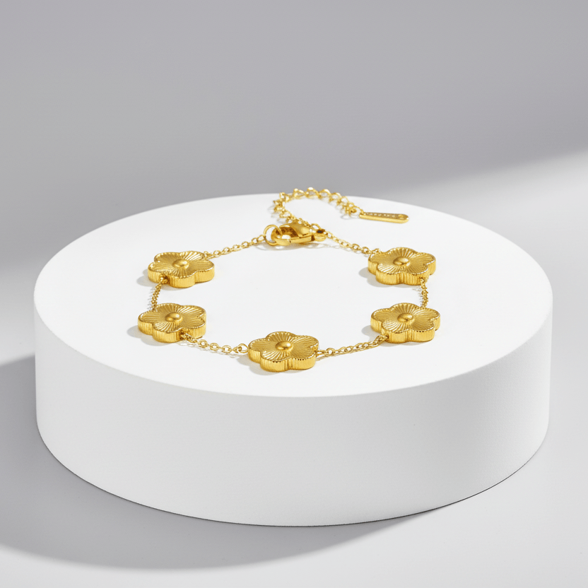Gold necklace with floral designs on a white pedestal against a gray background