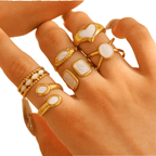 Hand wearing multiple gold rings with white stones on a light background