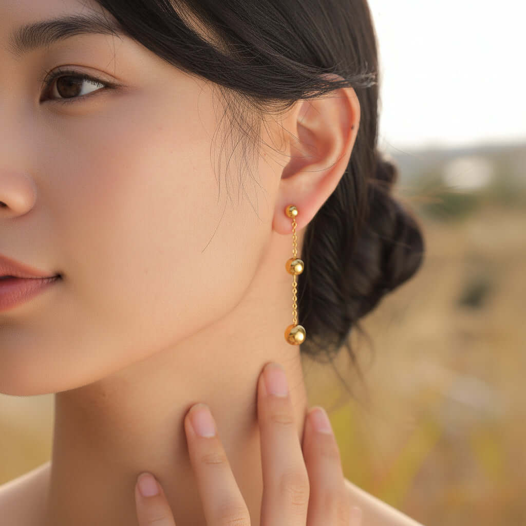 Close-up of a person Gold Ball Tassel Earrings with a blurred natural background