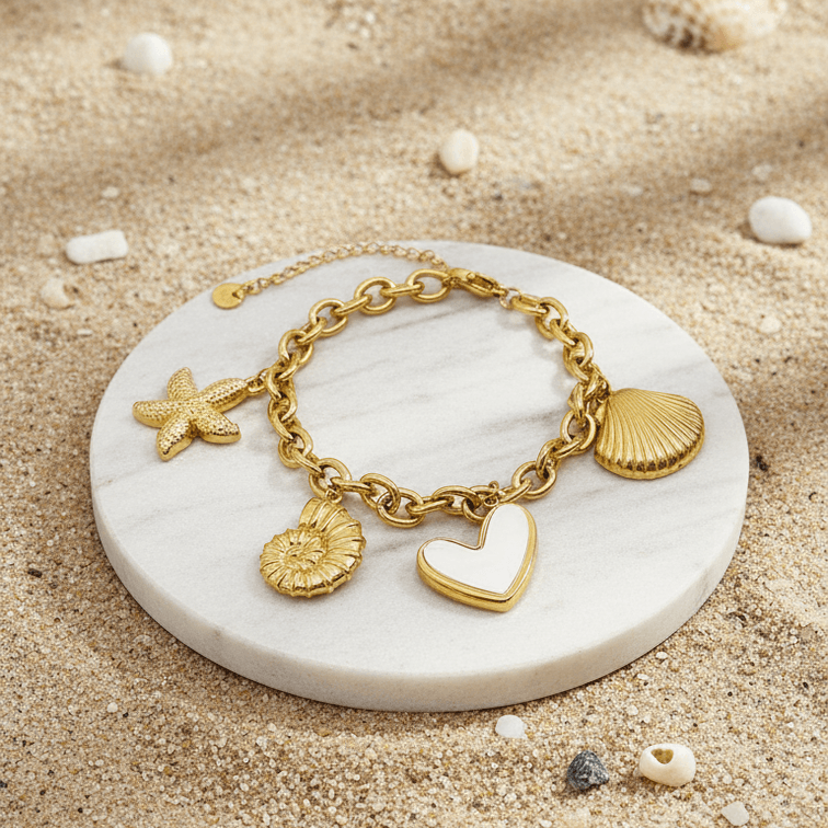 Gold Coastal Charm Bracelet on a white stone with seashells and sand in the background