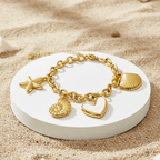 Gold bracelet with heart and shell charms on a white dish in sand