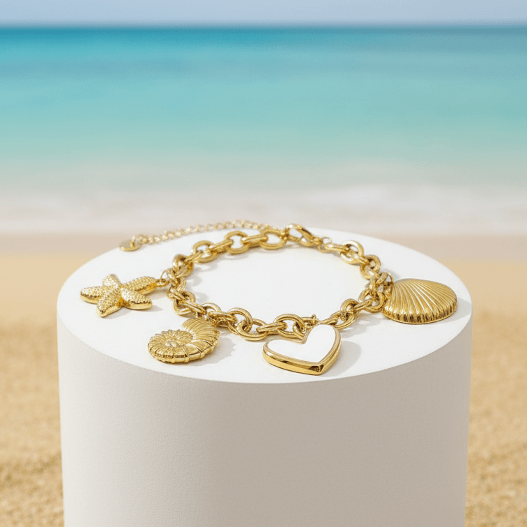 Gold charm bracelet on a white cylindrical stand with a beach background