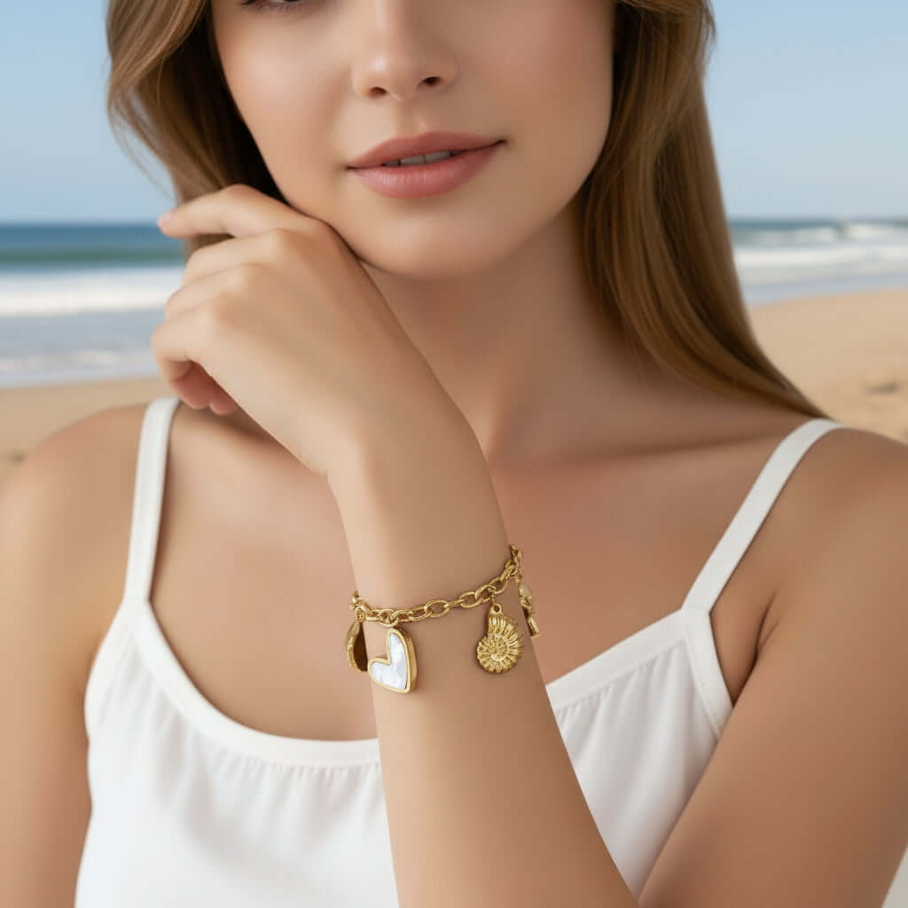 Gold Coastal Charm Bracelet with heart and shell charms on a person wearing a white top.