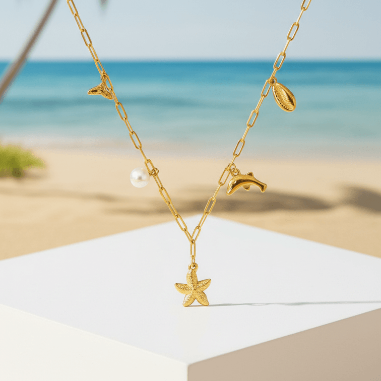 Gold Coastal Charm Necklace on white pedestal on beach
