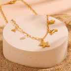 gold Coastal Charm Necklace with starfish and pearl charm on a beige stand with sand and shells in the background