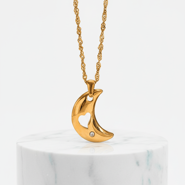 Gold necklace with a crescent moon pendant on a marble base