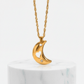 Gold necklace with a crescent moon pendant on a marble base