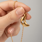 Gold necklace with a crescent moon pendant held by a hand against a gray background