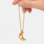 Gold crescent moon necklace held by a hand on a white background