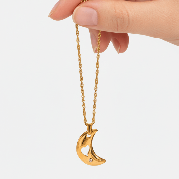 Gold crescent moon necklace held by a hand on a white background