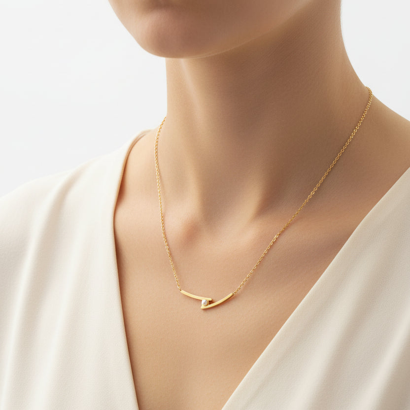 A Gold Cross Dainty Pearl Necklace with a curved bar pendant and a small clear stone, displayed on a black jewelry bust.