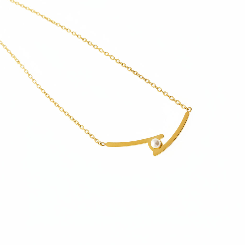 A gold Gold Cross Dainty Pearl Necklace resting on a gray laptop surface next to an Intel sticker.