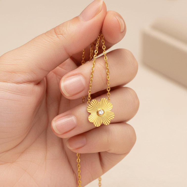 Gold Flower Pendant Necklace held by a hand against a neutral background