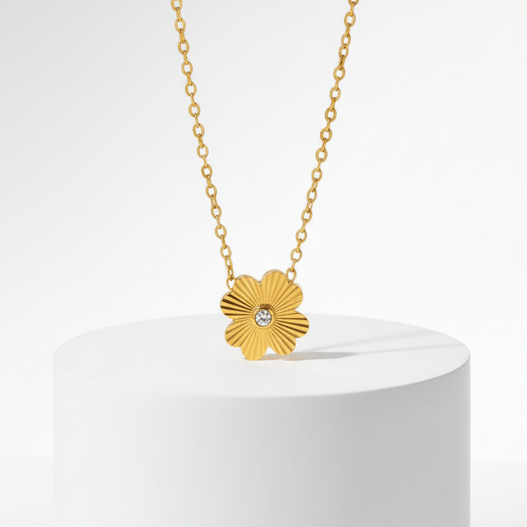 Gold Flower Pendant Necklace with a flower-shaped pendant on a white pedestal against a light gray background