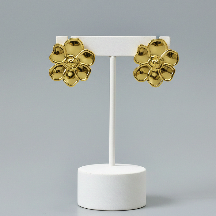A pair of Gold Flower Stud Earrings displayed on a white T-stand against a light gray studio background.
