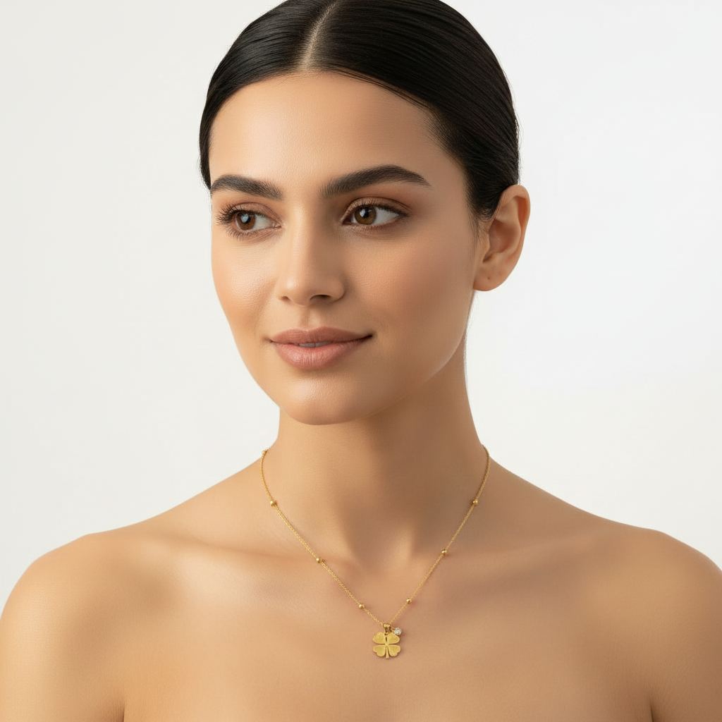 A close-up of a woman with dark hair pulled back, wearing a delicate gold chain necklace with a small gold flower pendant, set against a clean, light gray studio background.