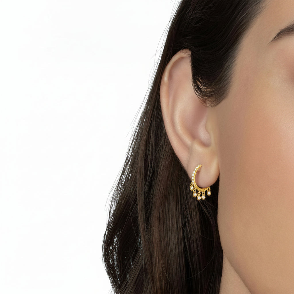 A close-up of a model's ear wearing a small Gold Gemstone Dangle Hoop Earrings, set against a solid light blue background.