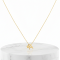 A delicate gold chain necklace with a small initial pendant featuring the letter 'A' and a small heart charm, displayed on a white marble cylinder pedestal against a white background.