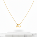 A delicate gold chain necklace featuring a small letter 'C' pendant and a small heart charm, displayed on a white marble block against a clean white background.