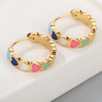 Gold hoop earrings with colorful heart-shaped stones on a wooden surface