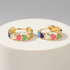Gold Heart Charm Hoop Earrings with colorful circular accents on a white stand against a gray background