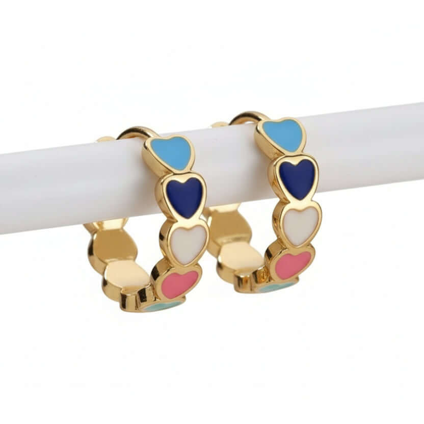 Gold Heart Charm Hoop Earrings with colorful heart charms on a wooden stick against a beige background