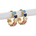 Gold Heart Charm Hoop Earrings with colorful heart charms on a wooden stick against a beige background