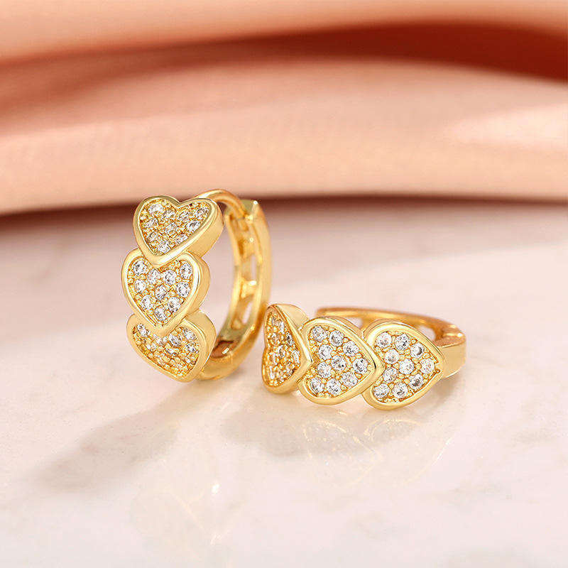 Gold Heart Crystal Cluster Hoop Earrings with clear stones on a light pink background