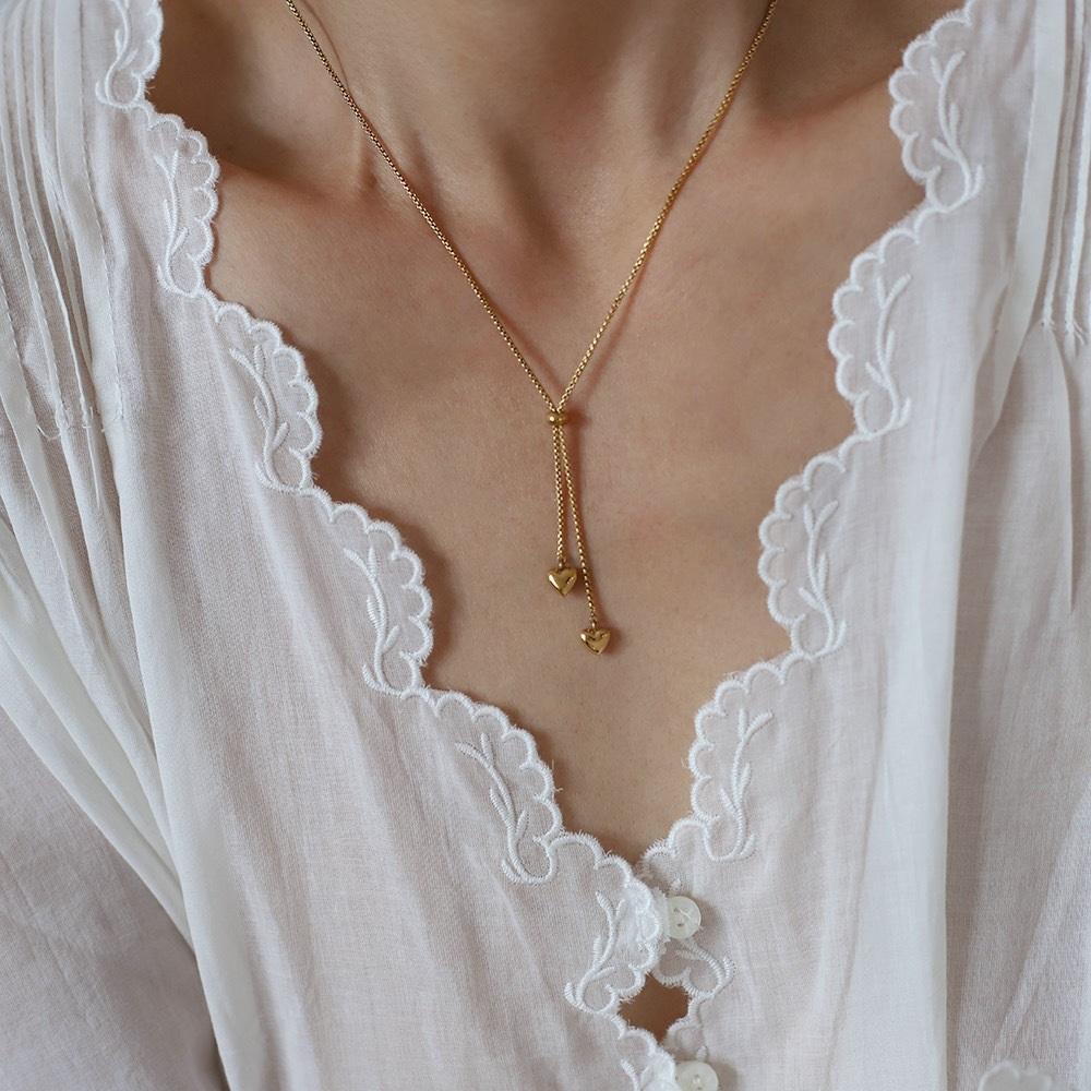 A close-up of a model wearing a delicate Gold Heart Drop Y Necklace Adjustable with two small dangling heart charms, styled with a white lace-trimmed blouse.