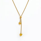 A Gold Heart Drop Y Necklace Adjustable featuring a textured chain, a central bead, and two dangling heart charms, shown on a plain white background.