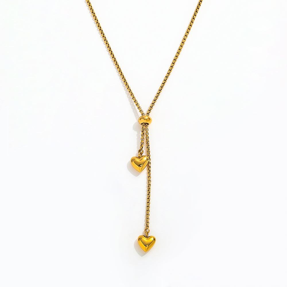 A Gold Heart Drop Y Necklace Adjustable featuring a textured chain, a central bead, and two dangling heart charms, shown on a plain white background.