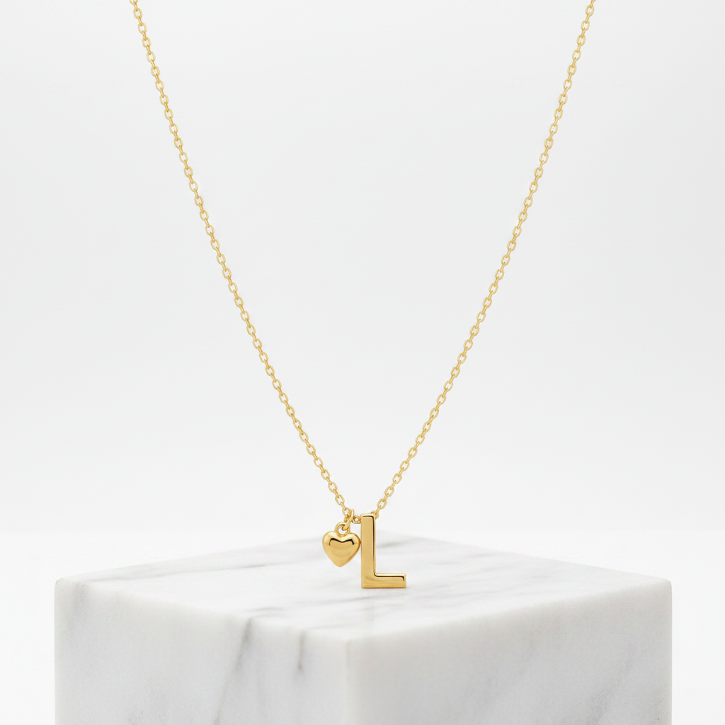 A delicate Gold Heart & I Initial Pendant Necklace, displayed on a white marble block against a clean white background.