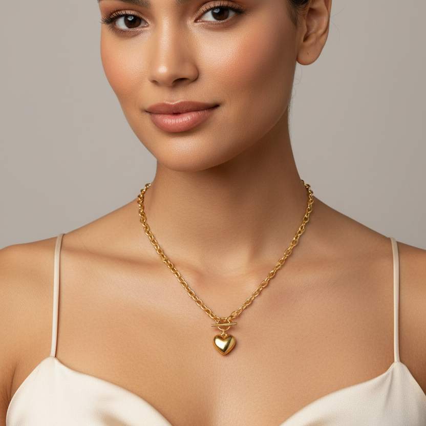 A close-up of a woman wearing a Gold Heart OT Toggle Necklace against a neutral gray background.
