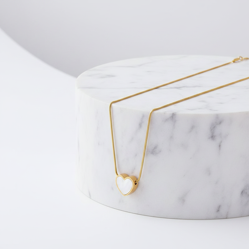 A delicate Gold Heart White Inlay Necklace draped over a white marble cylinder on a clean white background.
