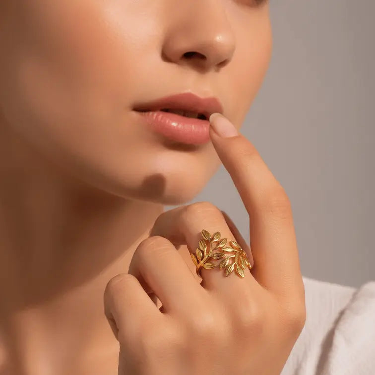 Close-up of a woman's hand with a Gold Leaf Branch Adjustable Ring on her finger, touching her lips against a neutral background.