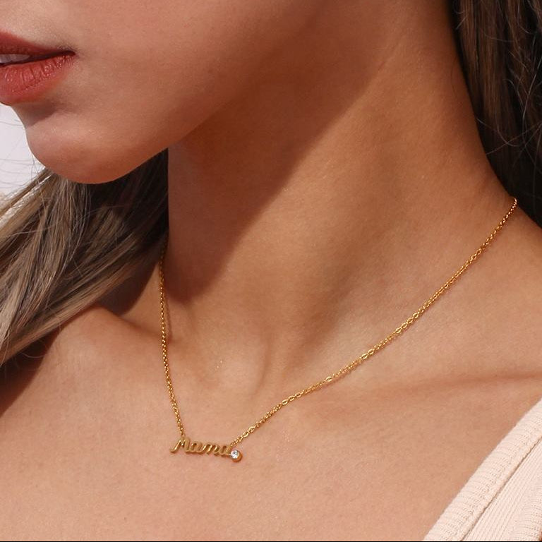 Close-up of a woman wearing a delicate Gold Mama Necklace With Rhinestone Detail and matching dangling gold hoop earrings with script lettering.